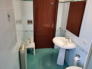 A compact bathroom with a sink, mirror, and toilet, featuring a tiled floor and a wooden door.