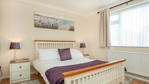 A bedroom with a bed, bedside tables, a nightstand, a window with curtains, and a painting on the wall. - A great, three-bedroom bungalow, with front and back gardens. (Warbstow, near Crackington Haven)