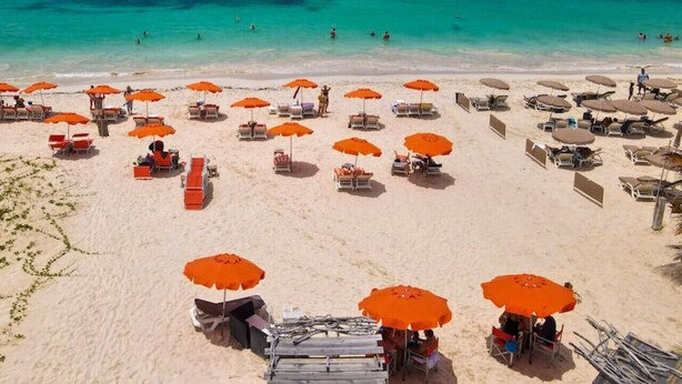 A beach with numerous orange umbrellas and sun loungers arranged in rows. - Maison Caraïbes, sur la plage d`Orient Bay (Orient Bay)