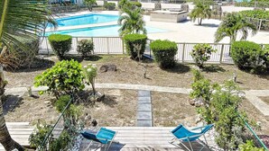 A pool area with a clear view of the ocean, surrounded by greenery and a wooden deck. - Maison Caraïbes, sur la plage d`Orient Bay (Orient Bay)