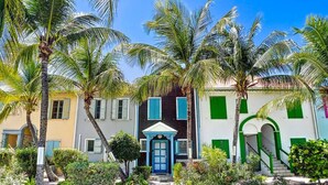 A two-story building with a blue door and green shutters, surrounded by palm trees and a well-maintained garden. - Maison Caraïbes, sur la plage d`Orient Bay (Orient Bay)