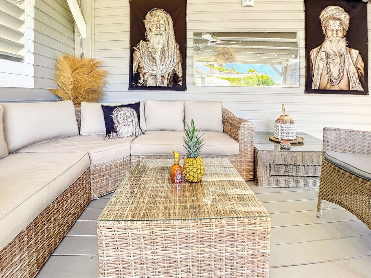 Un espacio exterior moderno con mobiliario de mimbre, una mesa central con una piña y una botella, y elementos decorativos.