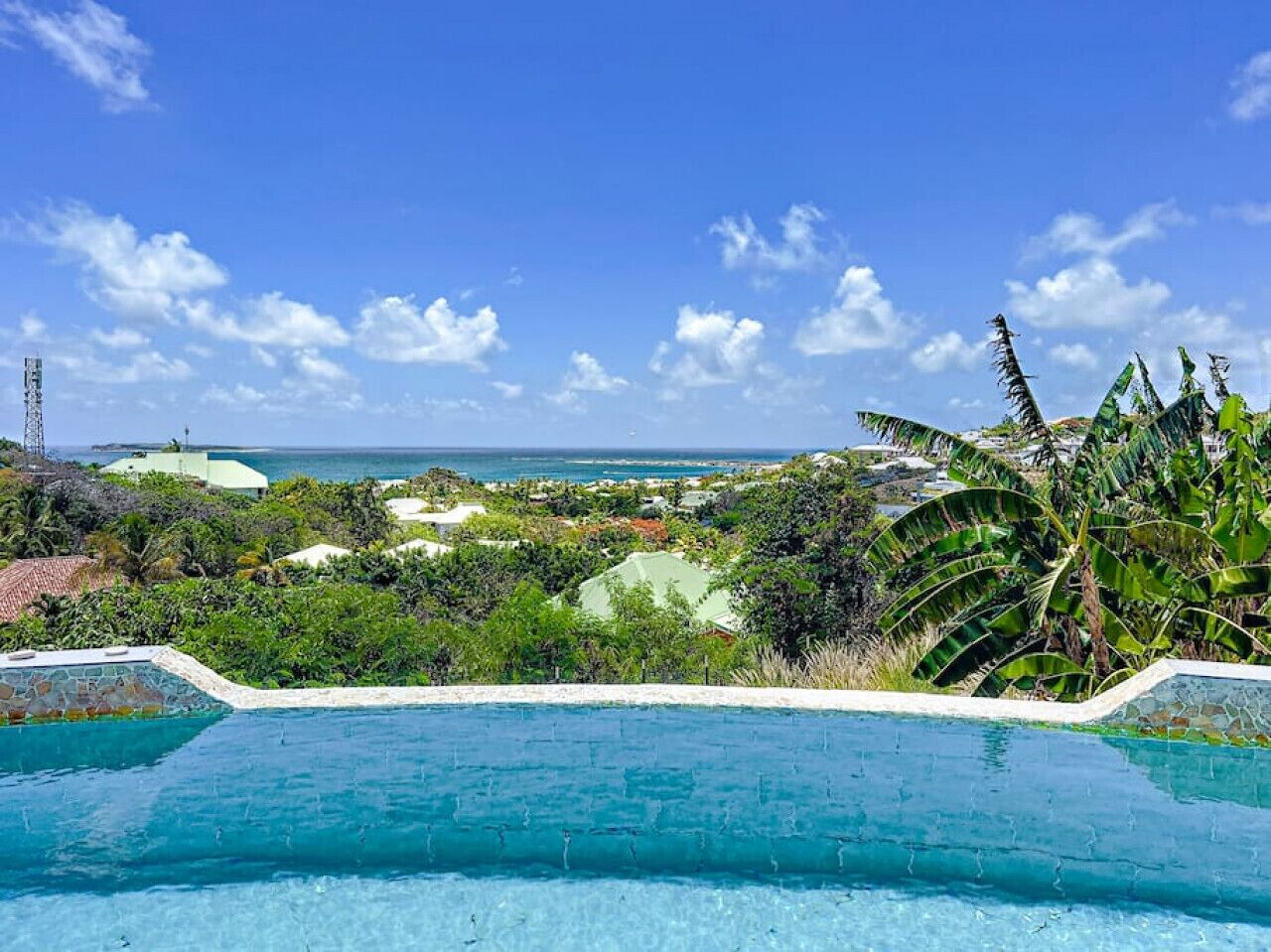 Une piscine avec vue sur l’océan et la végétation tropicale.