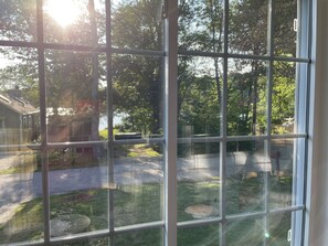 A view through a window with a grid pattern, revealing a backyard with a lawn, a tree, and a house in the background. - Lakeview property in private community. Lake & beach access. Swim/Kayak all day! (Bethlehem)