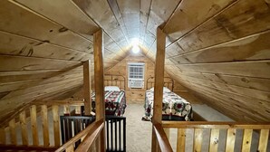 Ein Schlafzimmer im Dachgeschoss mit Holzbalken, geneigter Decke, einem zentralen Fenster und einem kleinen Tisch mit Stühlen.