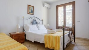 Un dormitorio con una cama, dos mesitas de noche, una lámpara de noche, un ventanal y un equipo de aire acondicionado.