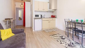Un espacio habitable compacto con kitchenette, comedor y sofá con un cojín amarillo.