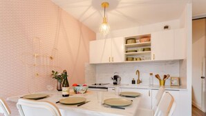 A modern kitchen with white cabinetry, a marble countertop, and a dining area with white chairs. - Le Clos Mathilde by Interhome (Cabourg)