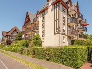 Um edifício residencial moderno, com vários andares, varandas e um jardim bem cuidado.
