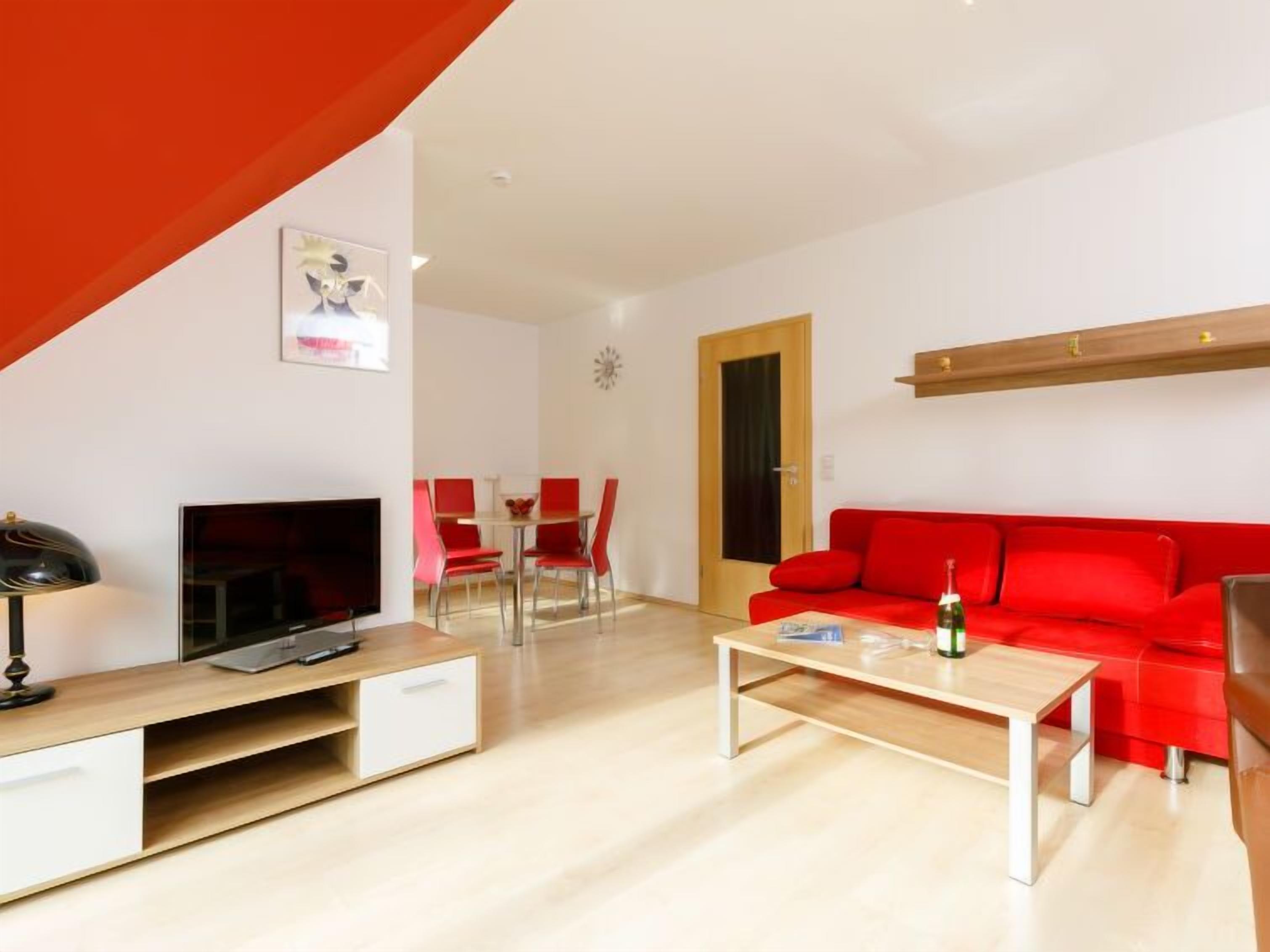 Un salon moderne avec un canapé rouge, un téléviseur et un coin repas avec des chaises rouges.