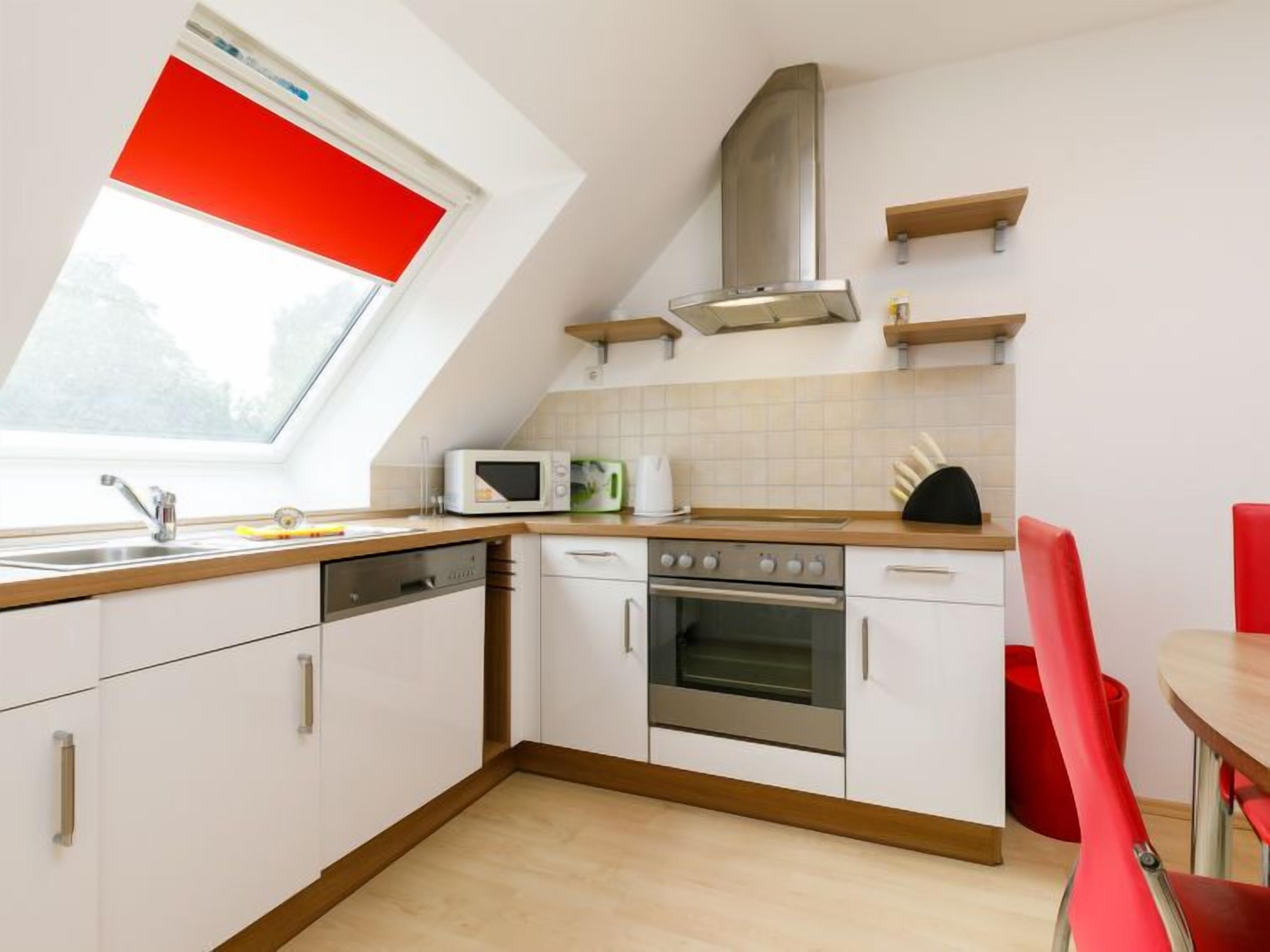A modern kitchen with white cabinets, a stainless steel oven, a microwave, and a red-framed window.