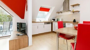 A modern kitchen with white cabinets, a red accent wall, a skylight, and a dining area with red chairs. - Apartment Preiss by Interhome (Zinnowitz)