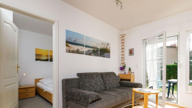 A modern living room with a grey sofa, a small wooden side table, and a door leading to another room. - Apartment Berg by Interhome (Zinnowitz)