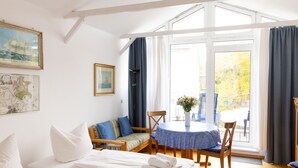 Ein Zimmer mit zwei Betten, einem Tisch mit Stühlen, einem Fenster mit Vorhängen und Blick ins Freie.