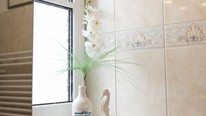 Eine Gin-Flasche, eine weiße Statue und eine weiße Orchidee auf einer gefliesten Fläche in der Nähe eines Fensters.