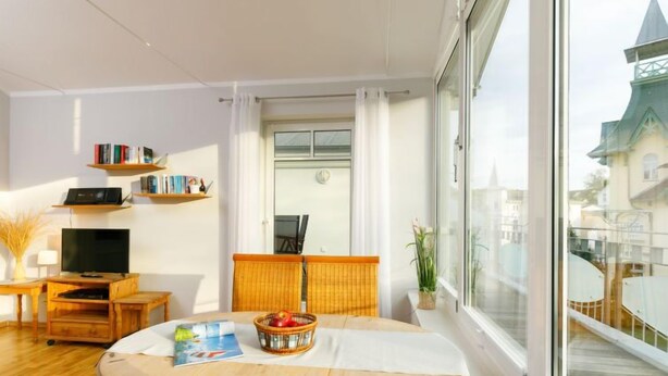 A modern living room with a large window, a television, bookshelves, and a dining area with a table and chairs. - Luise von Preußen (App. 205) by Interhome (Zinnowitz)