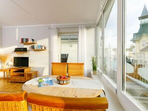 A modern living room with a large window, a television, bookshelves, and a dining area with a table and chairs. - Luise von Preußen (App. 205) by Interhome (Zinnowitz)