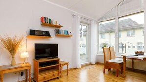 A living room with a TV, wooden furniture, bookshelves, and a view of the outside. - Luise von Preußen (App. 205) by Interhome (Zinnowitz)