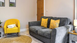 Una sala de estar con un sofá gris, un sillón amarillo y dos cuadros en la pared.
