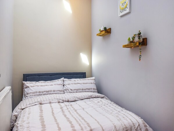 A bedroom with a bed, a radiator, and two wall-mounted shelves with plants.