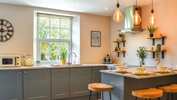 Una cocina moderna con armarios grises, una ventana con vistas, un reloj y luces colgantes.