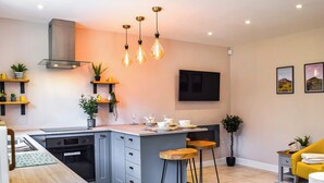 Una cocina moderna con una isla central, taburetes de bar, horno integrado y un televisor montado en la pared.