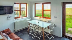 Eine kompakte Küche mit Esstisch und Stühlen, ein braunes Ledersofa und große Fenster mit Blick auf eine grüne Landschaft.