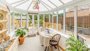 A conservatory with a dining table set for four, surrounded by chairs, and a large window offering a view of the garden.