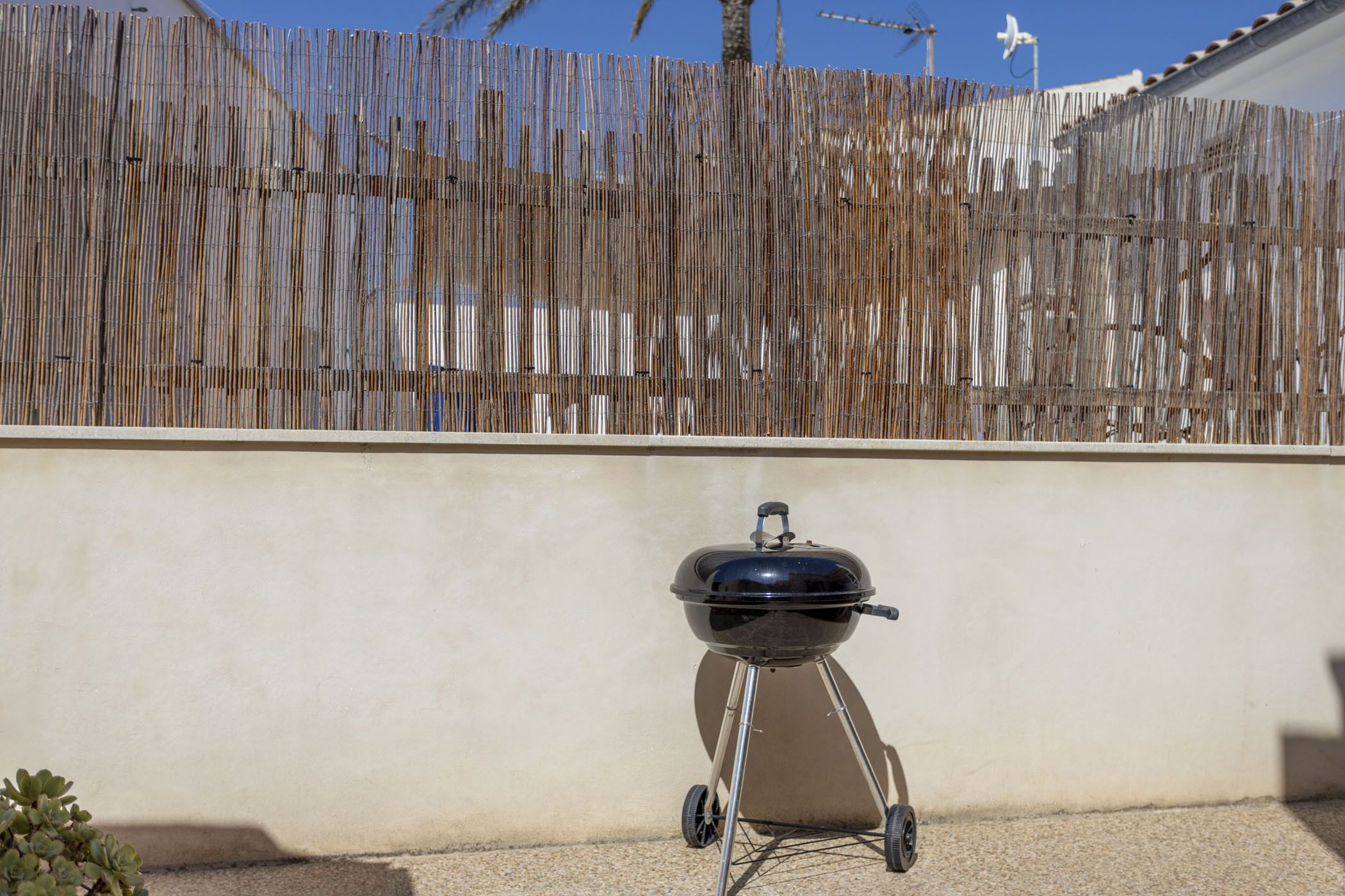 Un barbecue sur une terrasse, avec une clôture en bambou en arrière-plan.