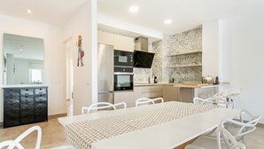 A modern kitchen with white cabinetry, a large dining table, and a TV mounted above the counter. - WELCS APARTAMENTO 078 EMP  con inmejorables vista (Empuriabrava)