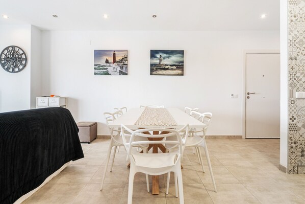 Une chambre moderne avec une table à manger blanche, des chaises blanches, un lit noir et deux tableaux encadrés accrochés au mur.