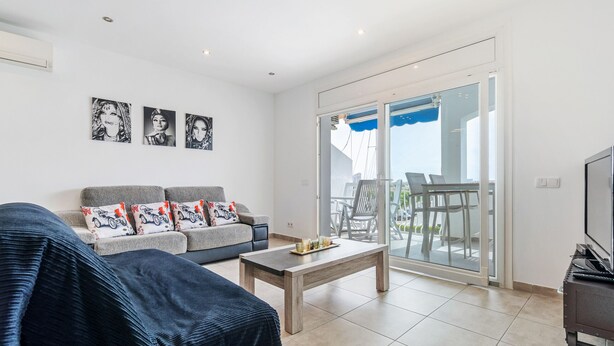 A modern living room with a sofa, a coffee table, and a TV stand. There is a sliding glass door leading to an outdoor area with a table and chairs. - WELCS APARTAMENTO 078 EMP  con inmejorables vista (Empuriabrava)