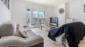 A modern living room with a sofa, a television, and a balcony with glass doors. - WELCS APARTAMENTO 078 EMP  con inmejorables vista (Empuriabrava)