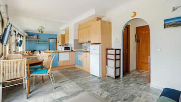 A compact kitchen with wooden cabinets, a dining area with wicker chairs, and a marble floor.