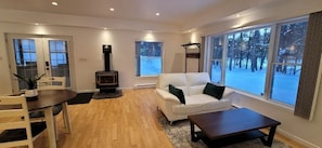 Relax in this stylish living room with a sofa, coffee table, and dining area, featuring a fireplace and a large window with a scenic view.