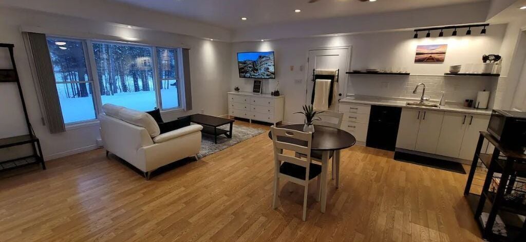 Un salon moderne avec un canapé blanc, une table à manger et un coin cuisine doté de meubles blancs et d’un évier.