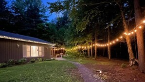 A wooden cabin with string lights, a paved path, and a grassy yard. - The Muskoka Room Huntsville with Hot Tub (Huntsville)