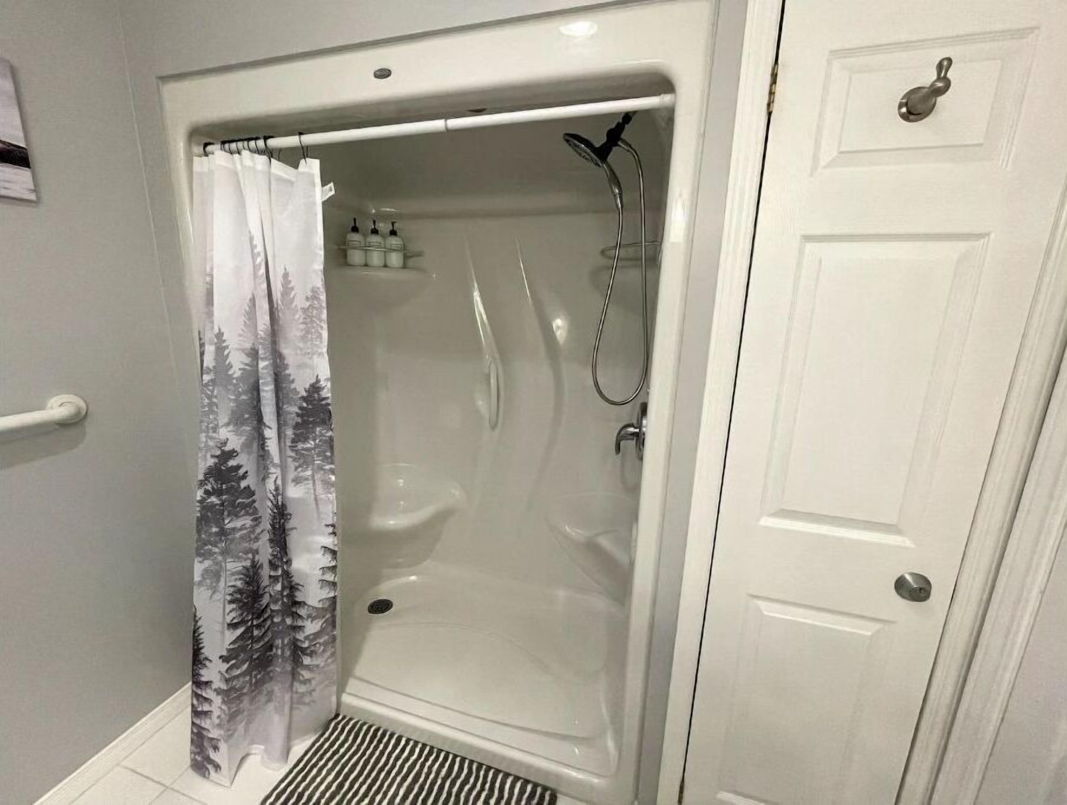 Eine barrierefreie Dusche mit Duschkopf, Vorhang und einer kleinen Ablage mit Flaschen.