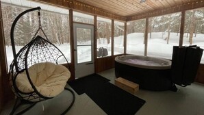 A cozy room with a hanging chair, a hot tub, and large windows overlooking a snowy landscape. - The Muskoka Room Huntsville with Hot Tub (Huntsville)