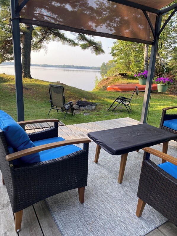 An outdoor patio with wicker furniture, a table, and a view of a lake.