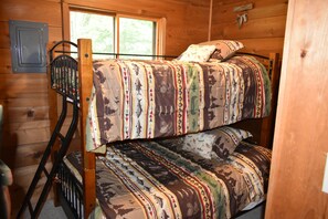 A bunk bed with patterned bedding in a cabin-style room with wooden walls and a window.