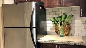 Une cuisine avec des meubles de rangement en bois foncé, un réfrigérateur en acier inoxydable et un plan de travail agrémenté d’une plante.