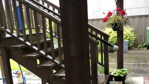 Un escalier en bois mène à une véranda abritée, agrémentée de plantes en pot et d’une jardinière suspendue.