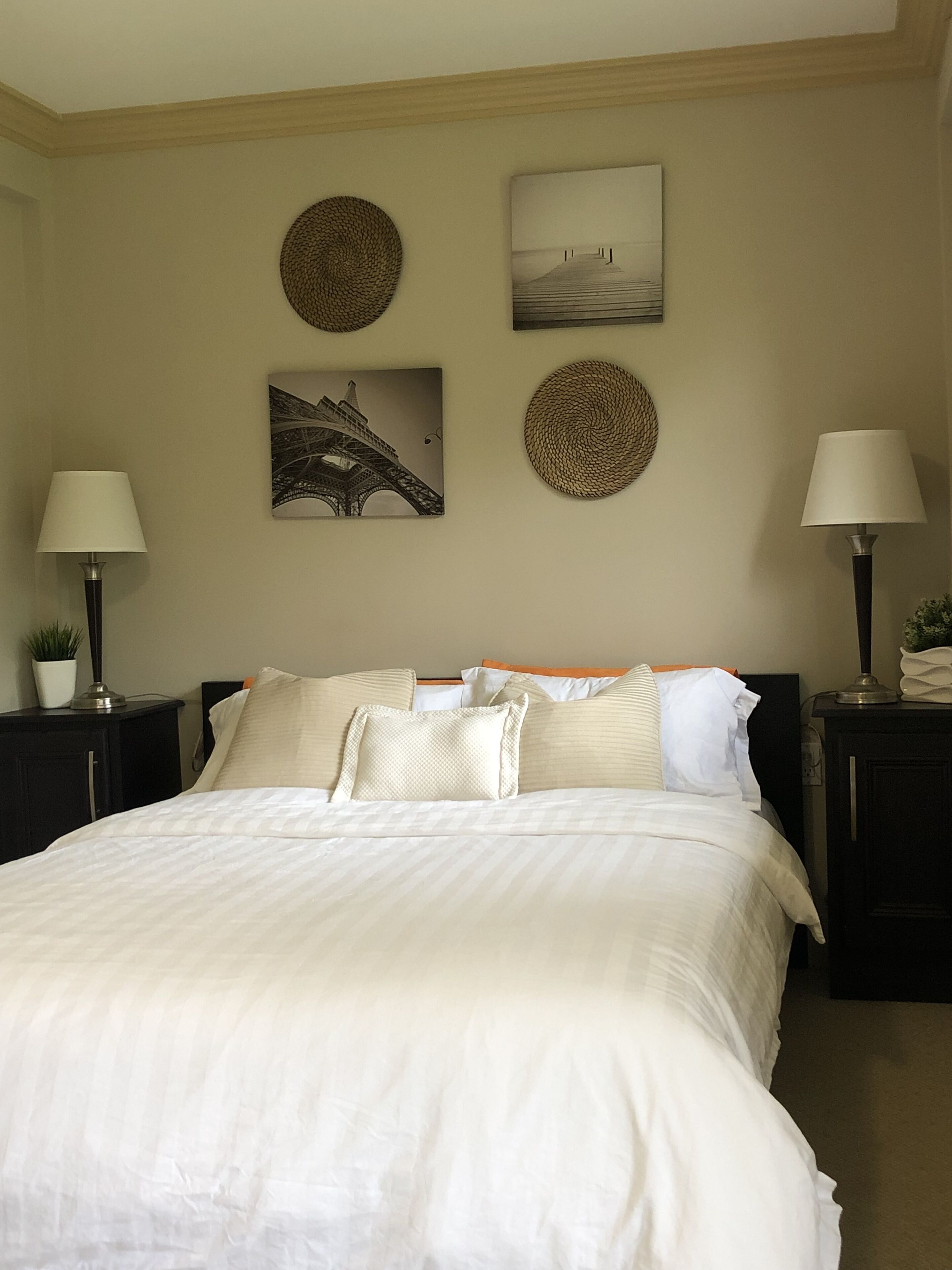 A neatly made bed with a white duvet and pillows, two bedside tables with lamps, and three wall-mounted artworks.