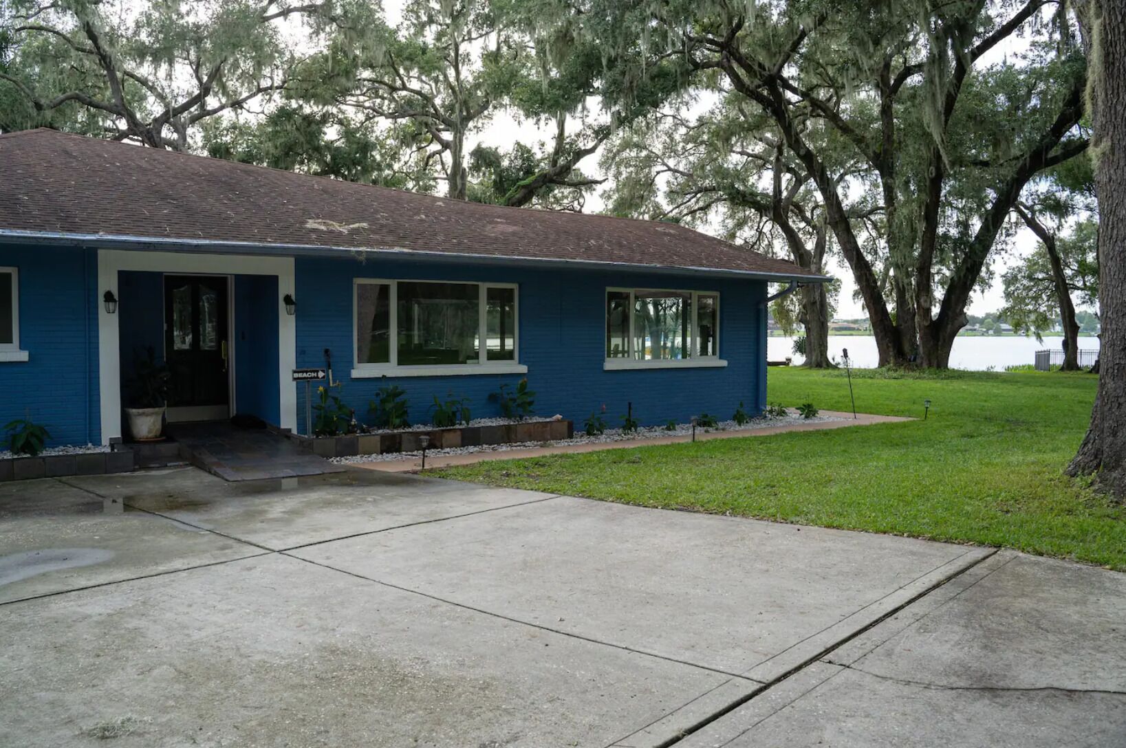 A single-story blue house with a front porch, a small front yard, and a view of a lake.