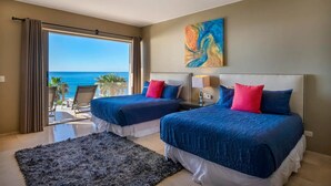 A hotel room with two beds, a large window with a view of the ocean, a ceiling fan, and a painting on the wall. - Villa Alegria (Cabo San Lucas)