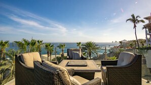 A terrace with outdoor furniture, a view of the ocean, and palm trees. - Villa Alegria (Cabo San Lucas)