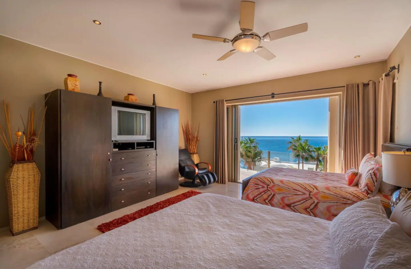 A hotel room with a large bed, a TV, a dresser, and a view of the ocean.