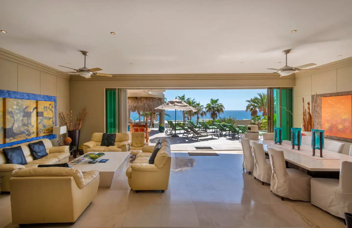 A spacious living room with a view of the ocean, beige sofas, a coffee table, and a dining area with chairs.