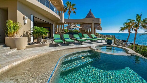 A resort with a pool, lounge chairs, and a view of the ocean. - Villa Alegria (Cabo San Lucas)